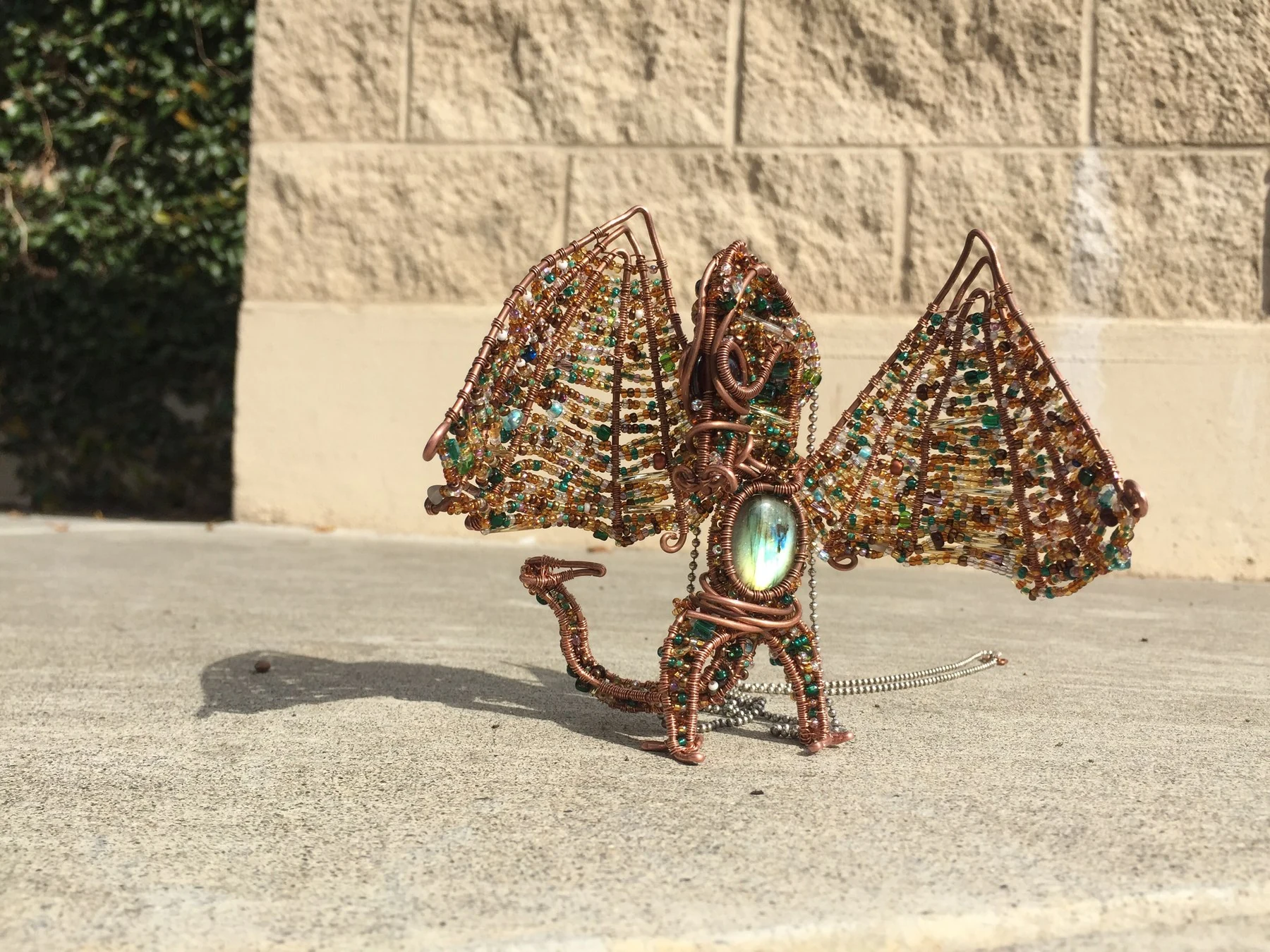 A handmade copper dragon standing in sunlight with its beaded wings spread.