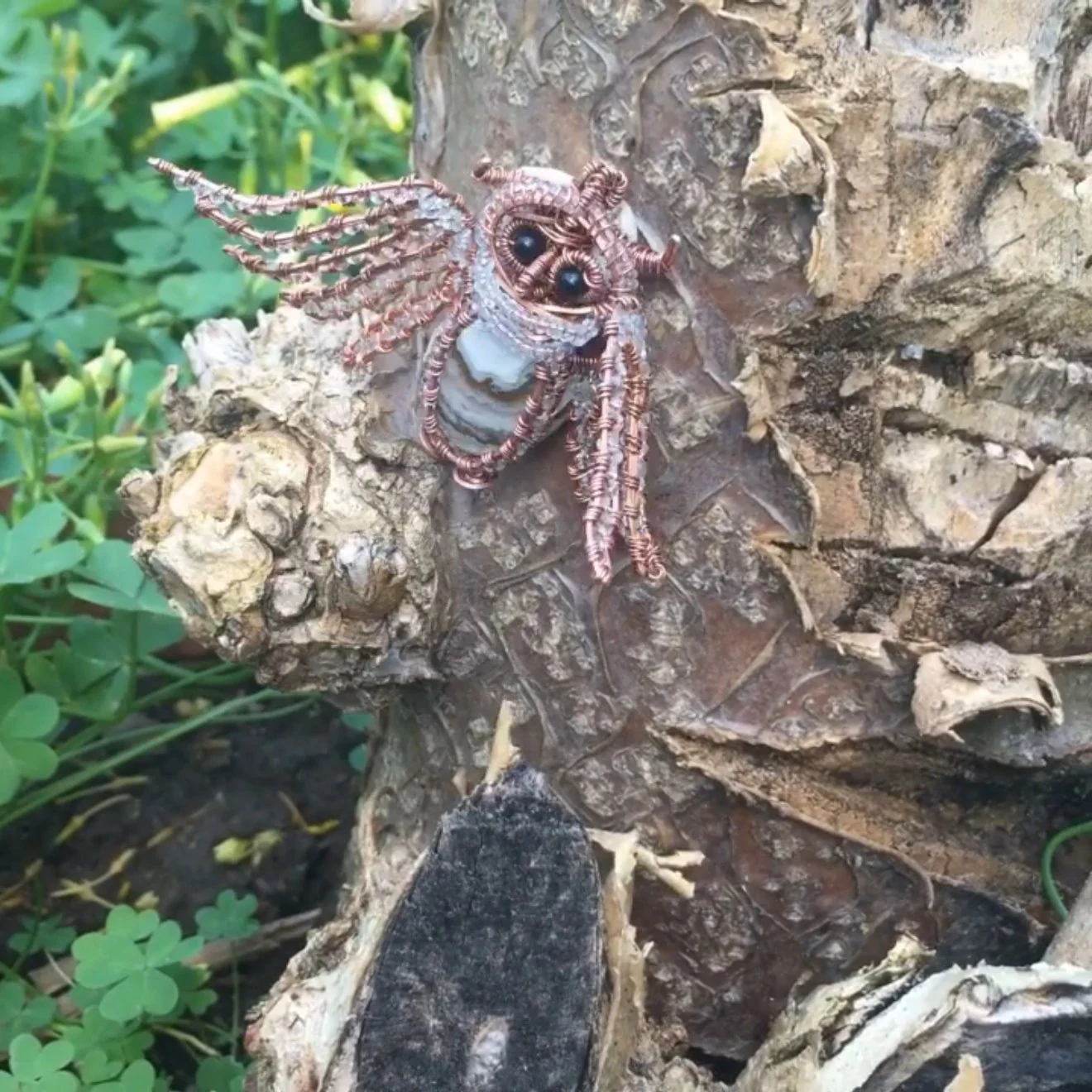 A wire-and-bead owl with spread wings hanging against a tree trunk.