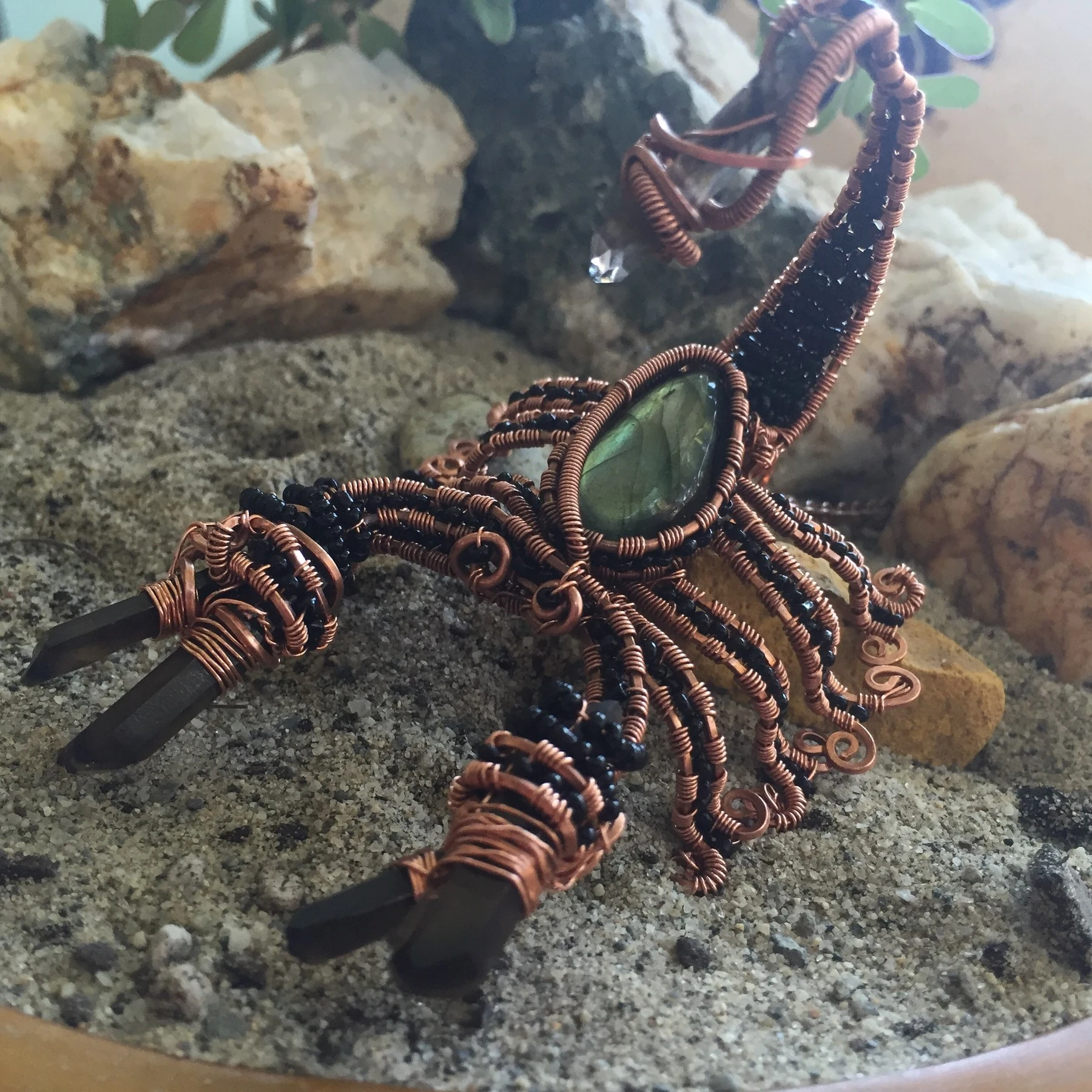 A copper-wire and beaded scorpion with stone claws and a raised tail, resting on rock.