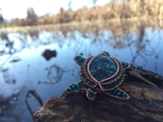 A small handmade turtle with a dark stone shell resting on wood beside water.